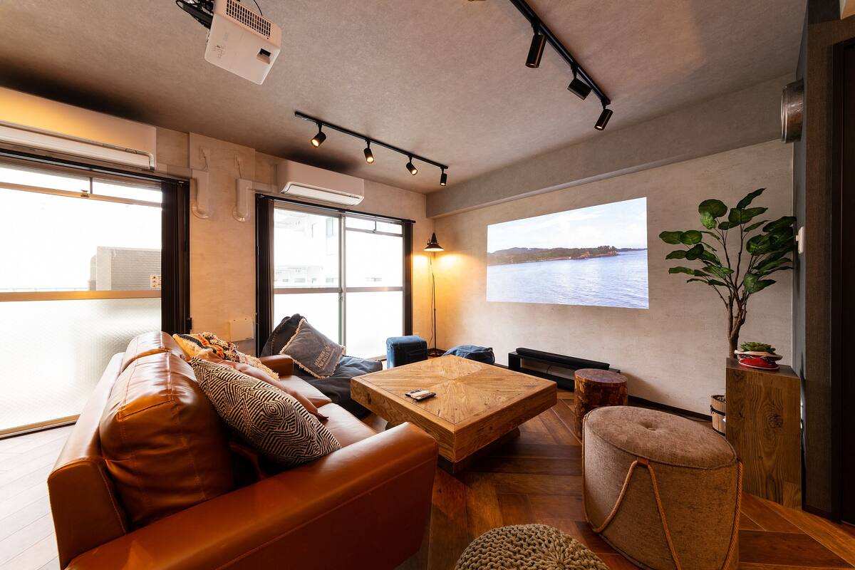 A modern living room with a leather sofa, a wooden coffee table, and a large window with a view of the water.