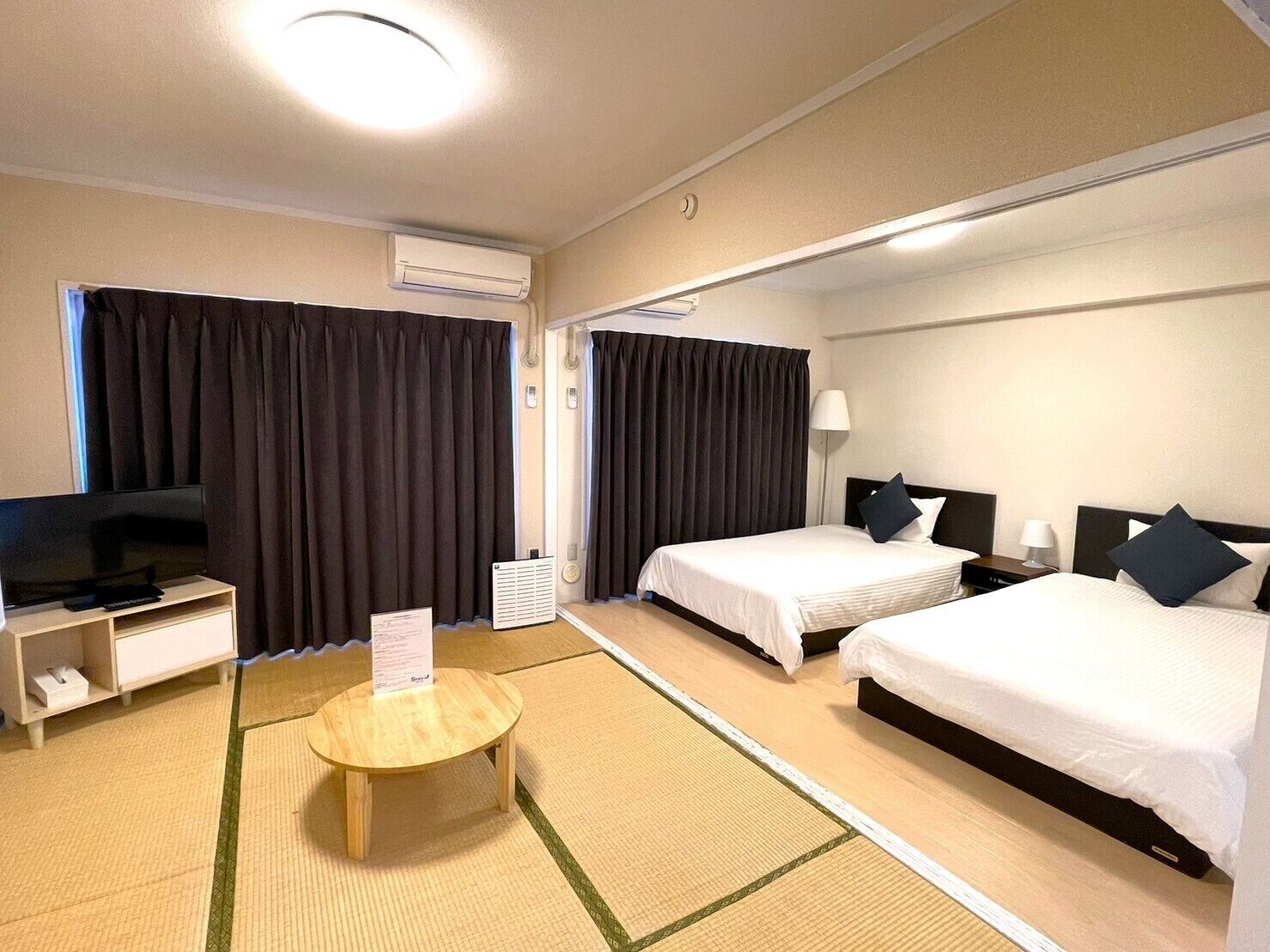 A hotel room with two beds, a TV, a bedside table, and a small round table with a placemat.