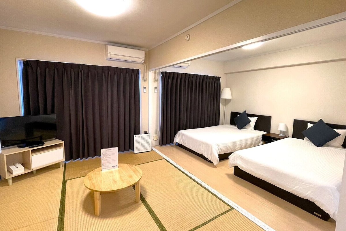 A hotel room with two beds, a TV, a bedside table, and a small round table with a placemat.