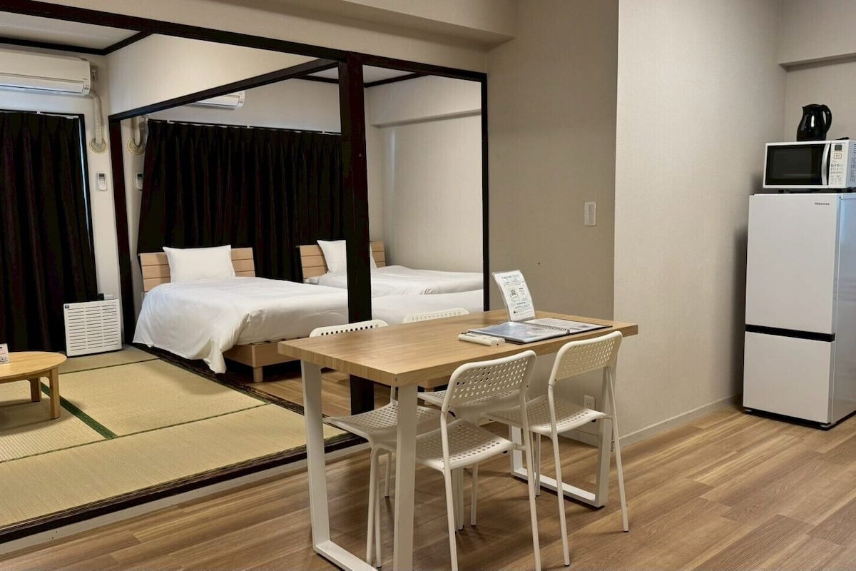 A hotel room with a bed, a desk with a chair, a microwave, a refrigerator, and a window.