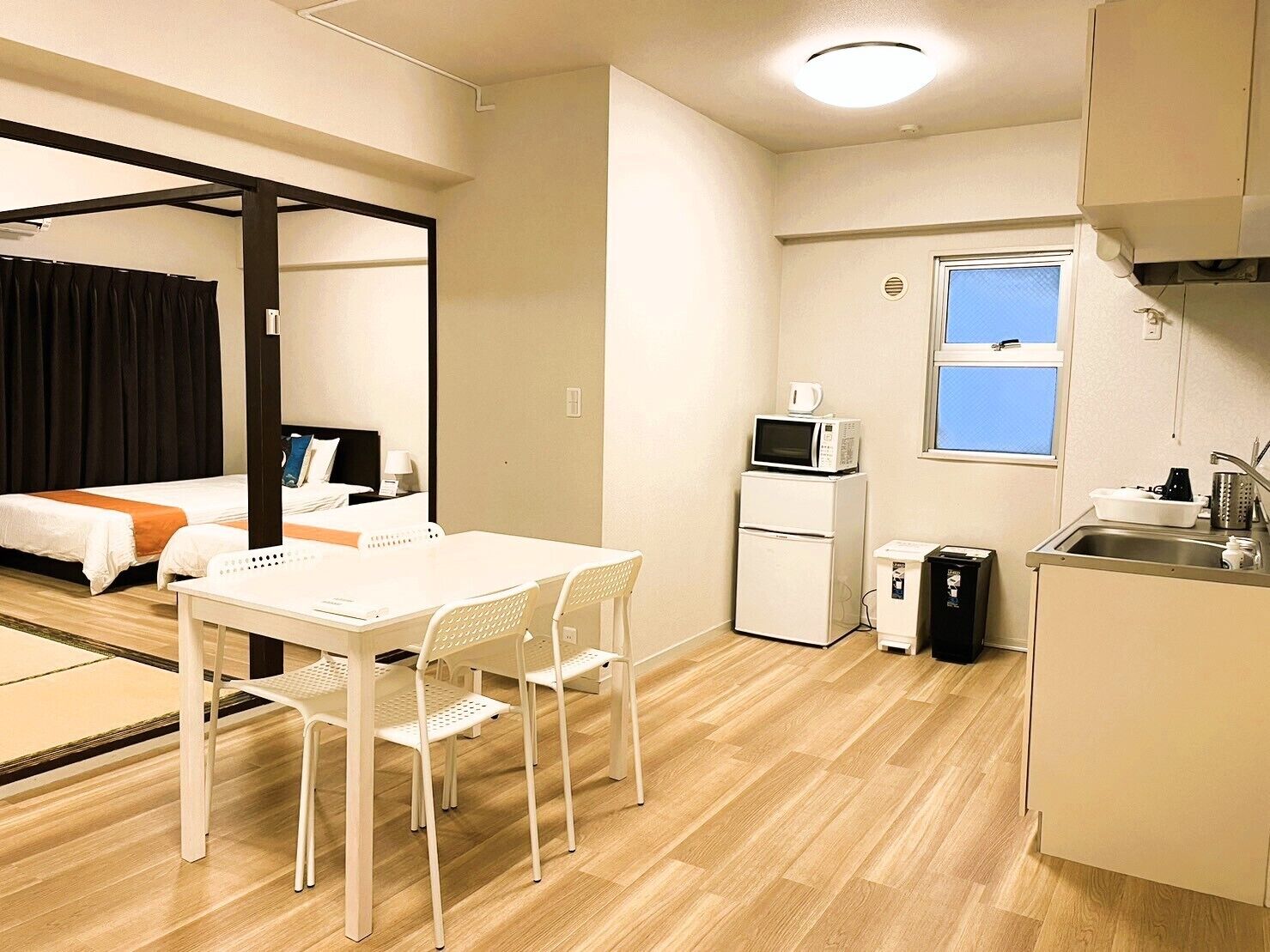 A compact hotel room with a bed, a small kitchenette, a dining area with a table and chairs, and a window.