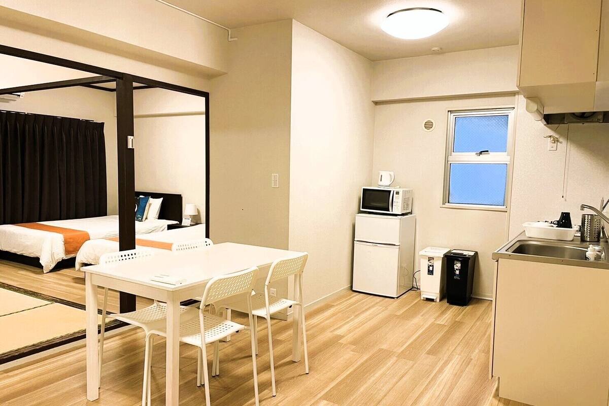 A compact hotel room with a bed, a small kitchenette, a dining area with a table and chairs, and a window.