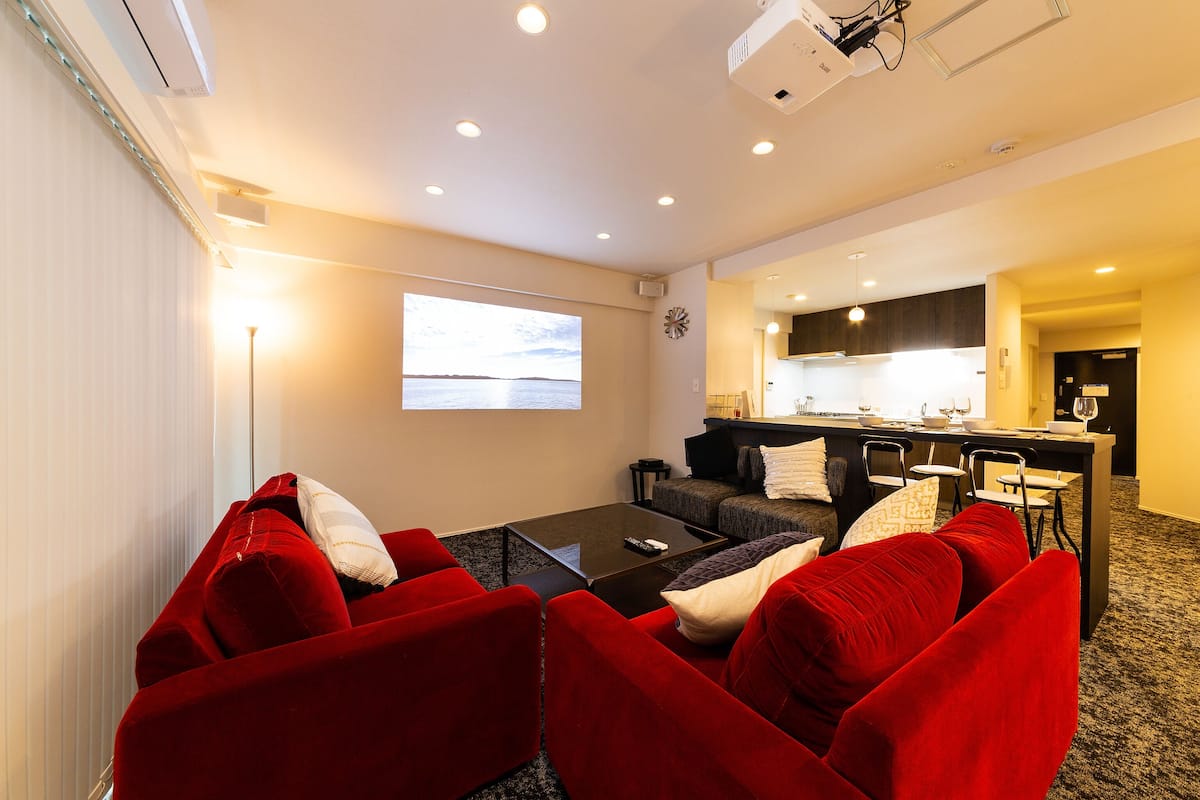 A modern living room with red sofas, a coffee table, and a large screen displaying a scenic view.