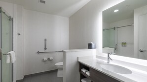 Un baño moderno con cabina de ducha de vidrio, inodoro blanco, tocador con lavamanos y espejo.