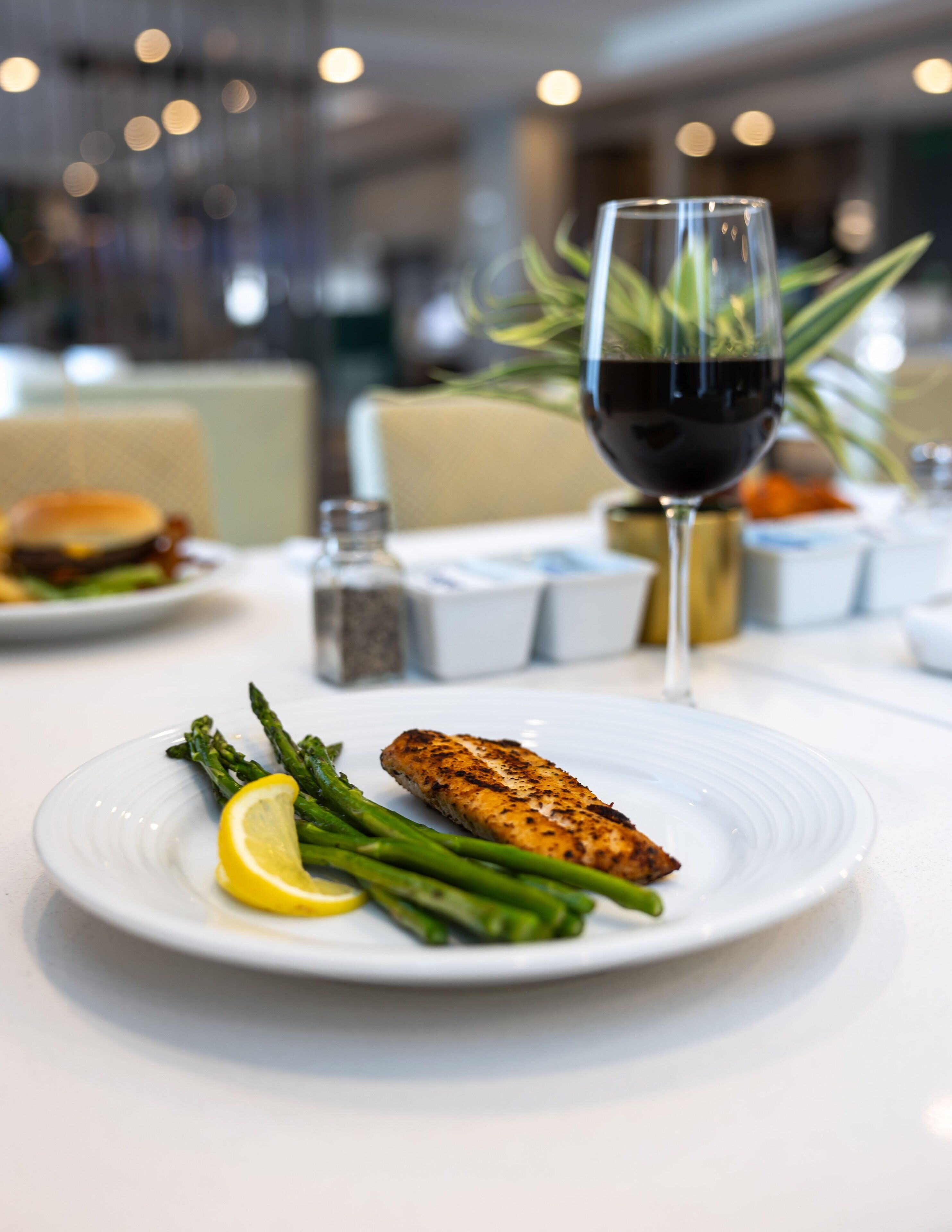 A plate with grilled fish, asparagus, and lemon on a white table in a restaurant setting.
