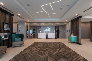 Un hall d’hôtel moderne comprenant un comptoir d’accueil, un espace salon et un tapis à motifs en chevrons.