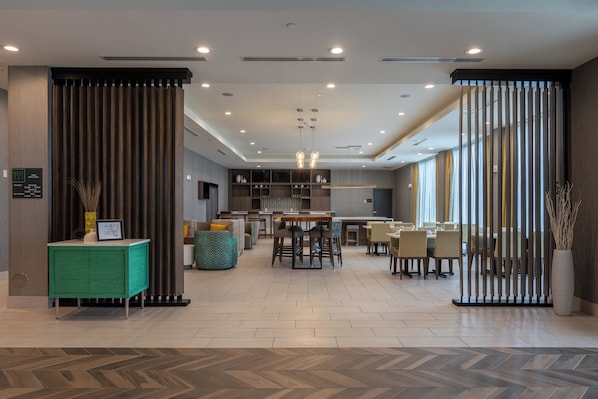 Un moderno vestíbulo de hotel con área de bar, asientos y mostrador de recepción.