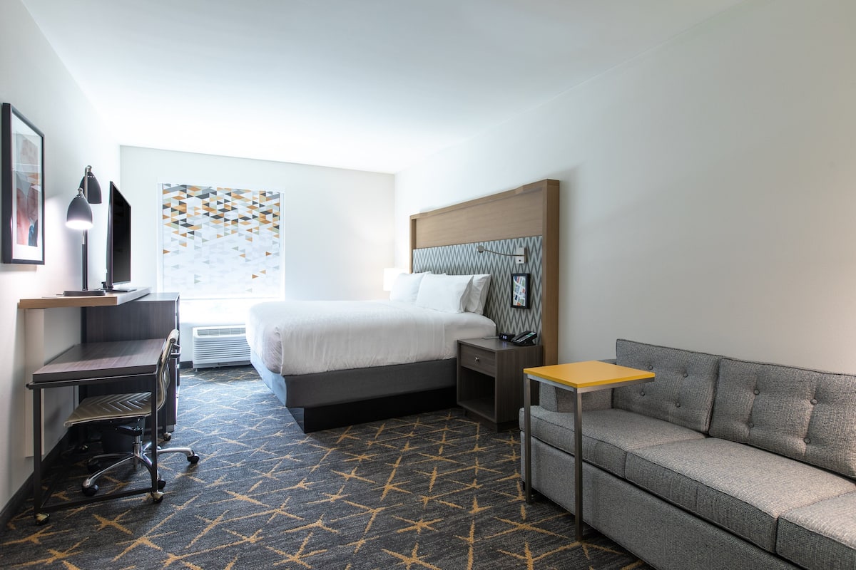 A hotel room with a bed, desk, chair, and a sofa.