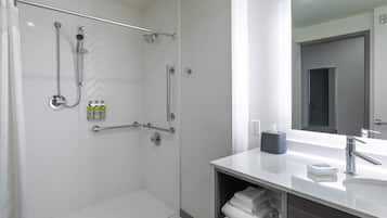 A modern bathroom with a walk-in shower, grab bars, a large mirror, and a vanity with a sink and towel rack.