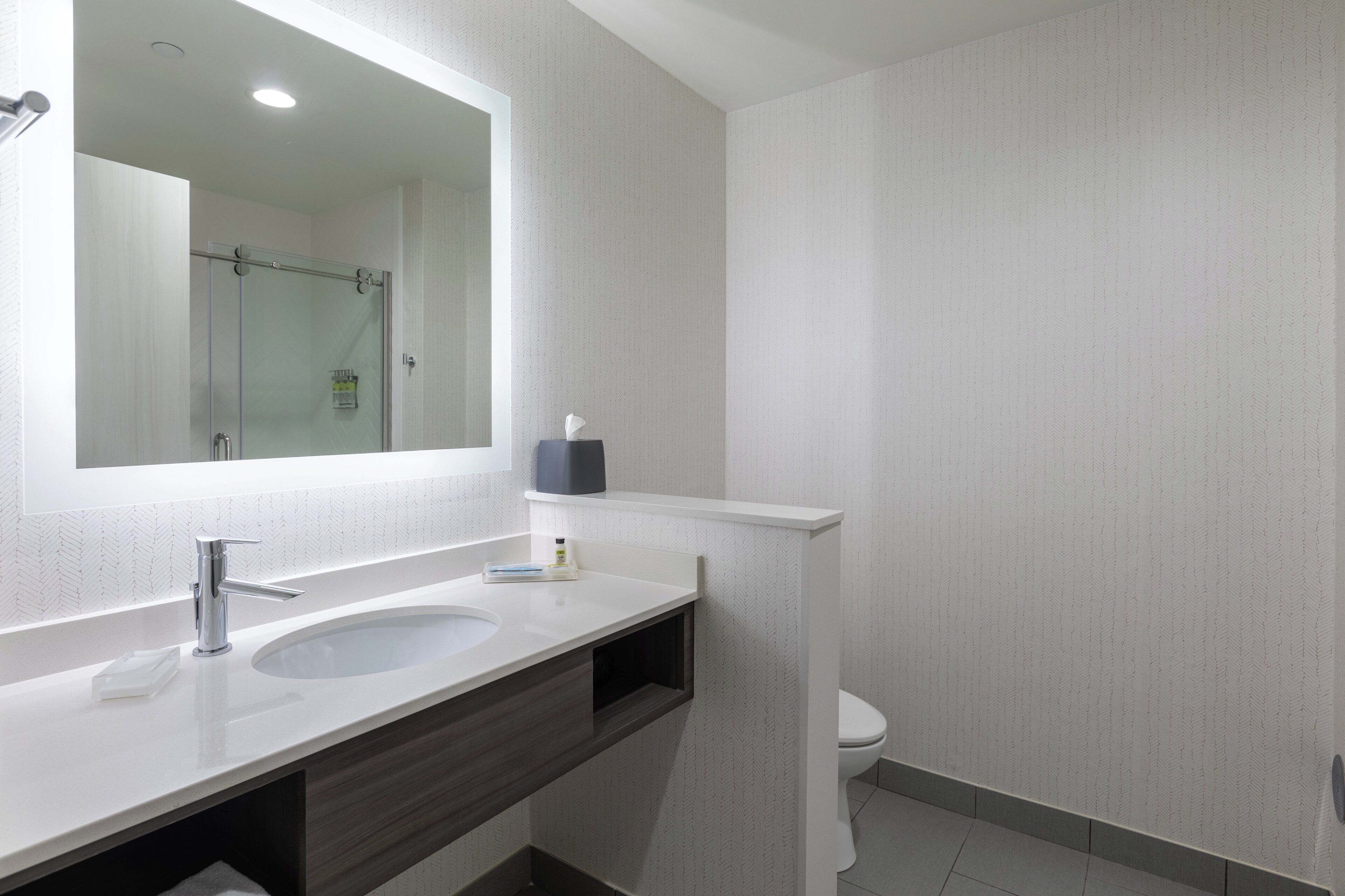 A modern bathroom with a large mirror, two sinks, a shower, and a toilet.