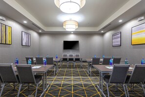 A conference room with a large flat-screen TV, multiple tables with chairs, and water bottles on each table. - Holiday Inn Greenville - Woodruff Road by IHG (Greenville)