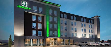 A Holiday Inn hotel with a modern design, featuring a prominent entrance and a parking lot with several vehicles.