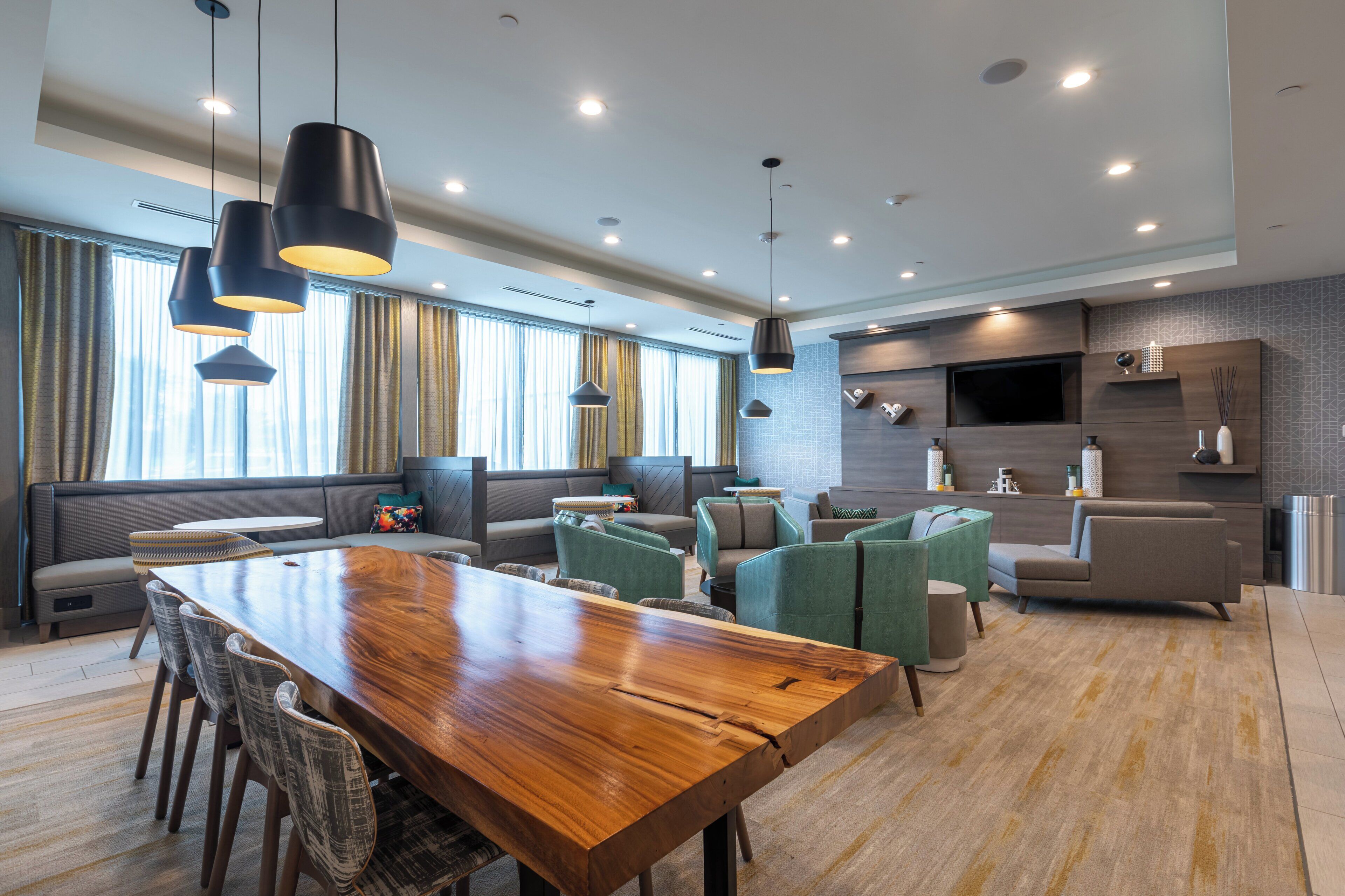 Une chambre d’hôtel moderne avec une table à manger en bois, des sièges confortables, un téléviseur à écran plat et une grande fenêtre avec des rideaux.