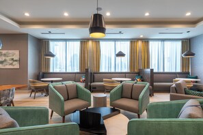 Espaço lounge moderno com assentos estofados em tons de verde, uma mesa de centro e iluminação pendente.
