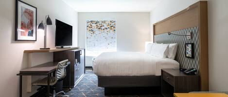 A hotel room with a bed, desk, chair, TV, and a window with a geometric pattern.