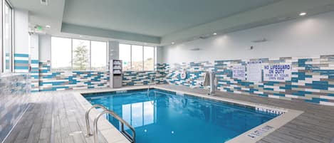 An indoor swimming pool with clear pool rules, a lifeguard chair, and a tiled wall with a view of the outside.