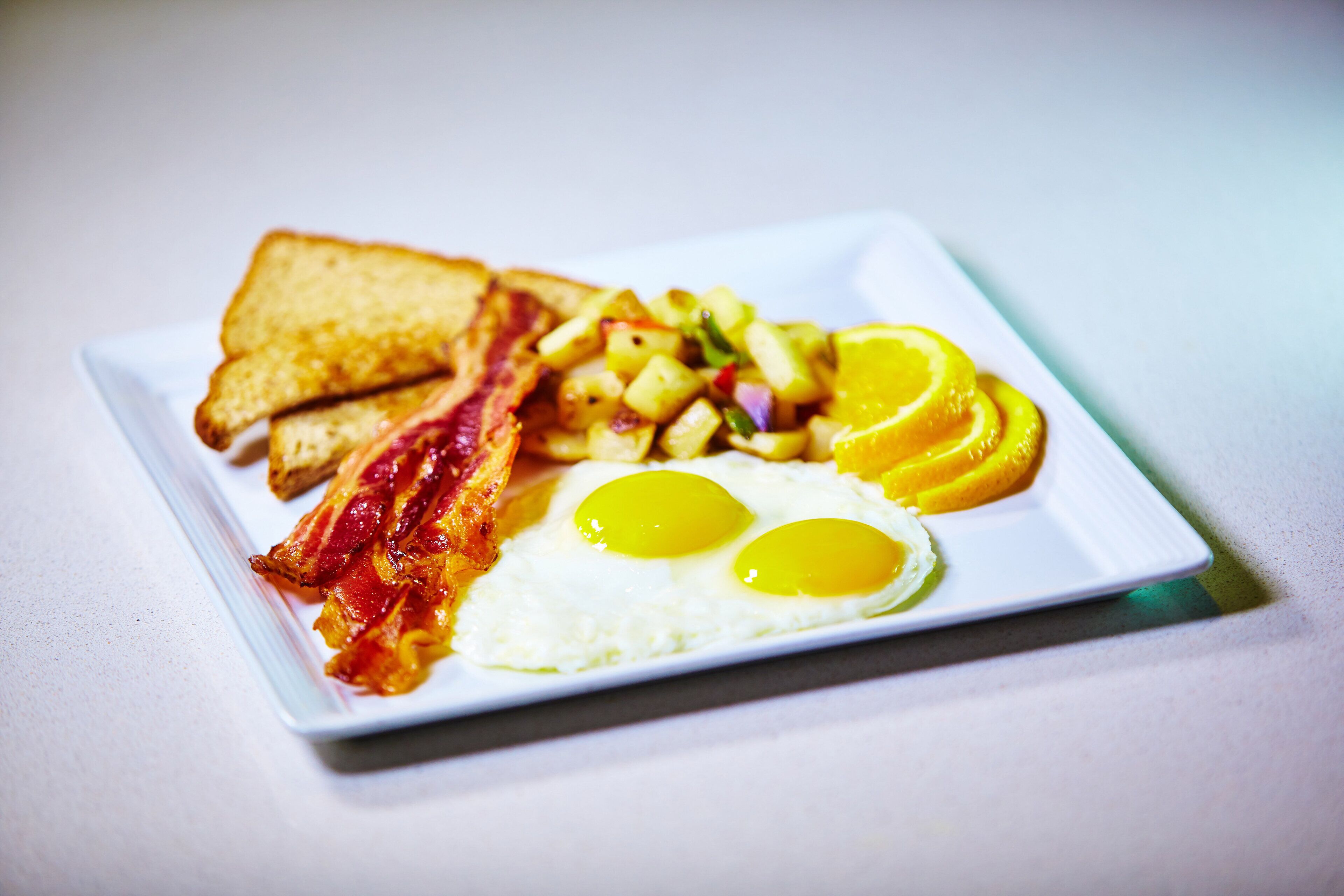 A plate with toast, bacon, eggs, and fruit.