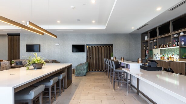 Una cocina moderna con barra, zona de estar con sofá y sillones, y televisor montado en la pared.