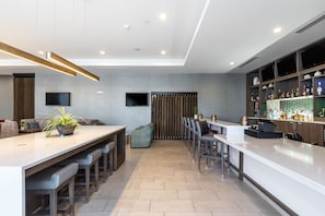 A modern kitchen with a bar area, a seating area with a sofa and chairs, and a television mounted on the wall. - Holiday Inn Greenville - Woodruff Road by IHG (Greenville)