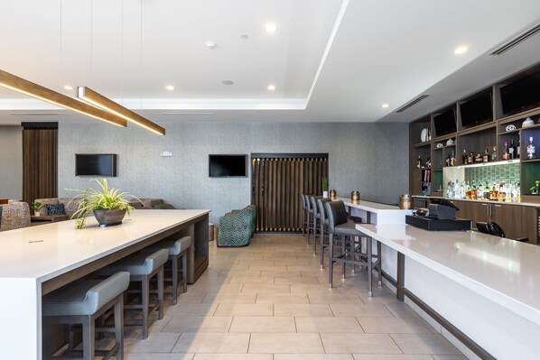 A modern kitchen with a bar area, a seating area with a sofa and chairs, and a television mounted on the wall.