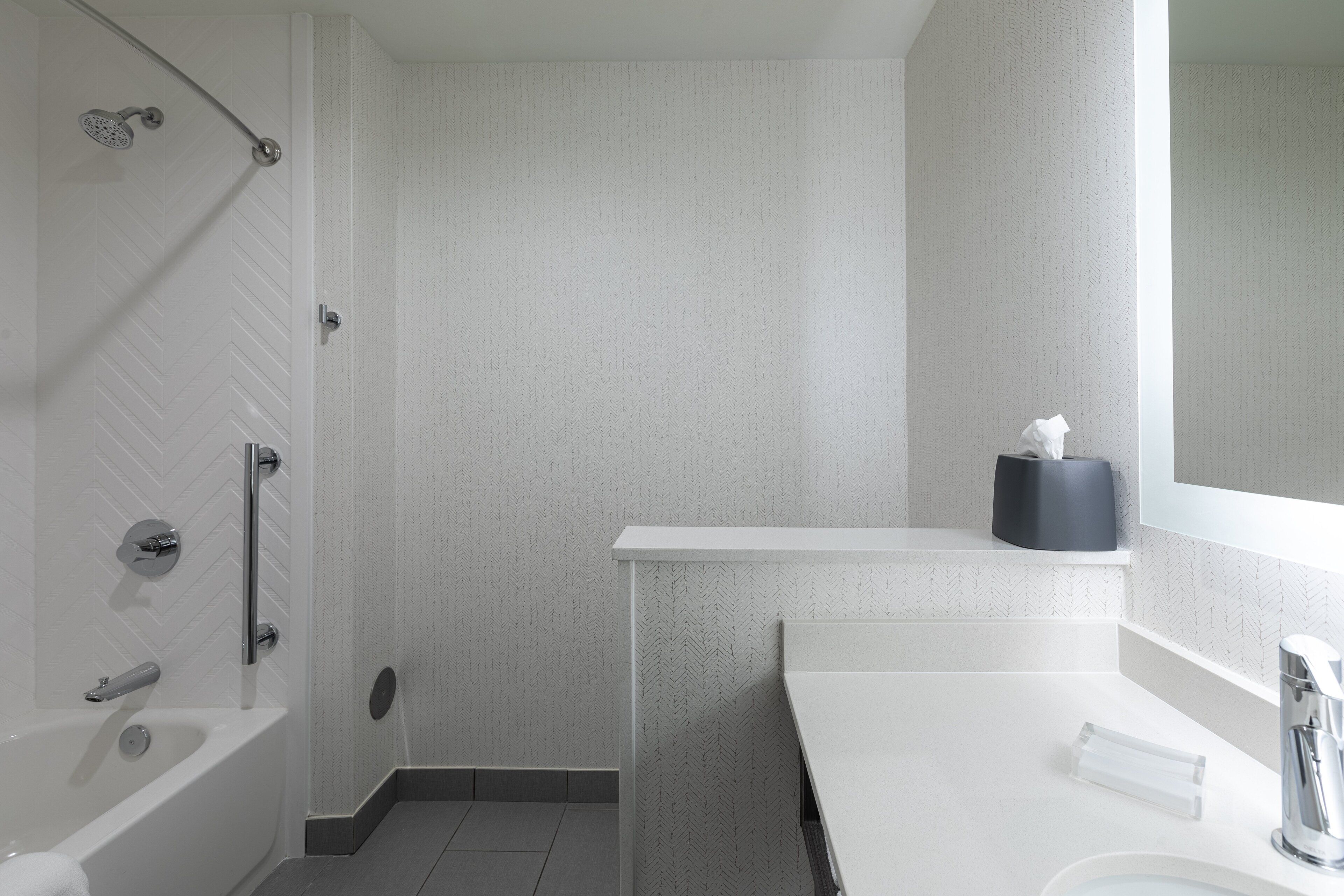 Une salle de bain moderne avec un meuble-lavabo blanc, une douche équipée d’un pommeau de douche à main et un porte-serviettes.