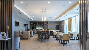 Un hall de hotel espacioso con una zona de bar central, arreglos de asientos y grandes ventanales que dejan entrar luz natural.