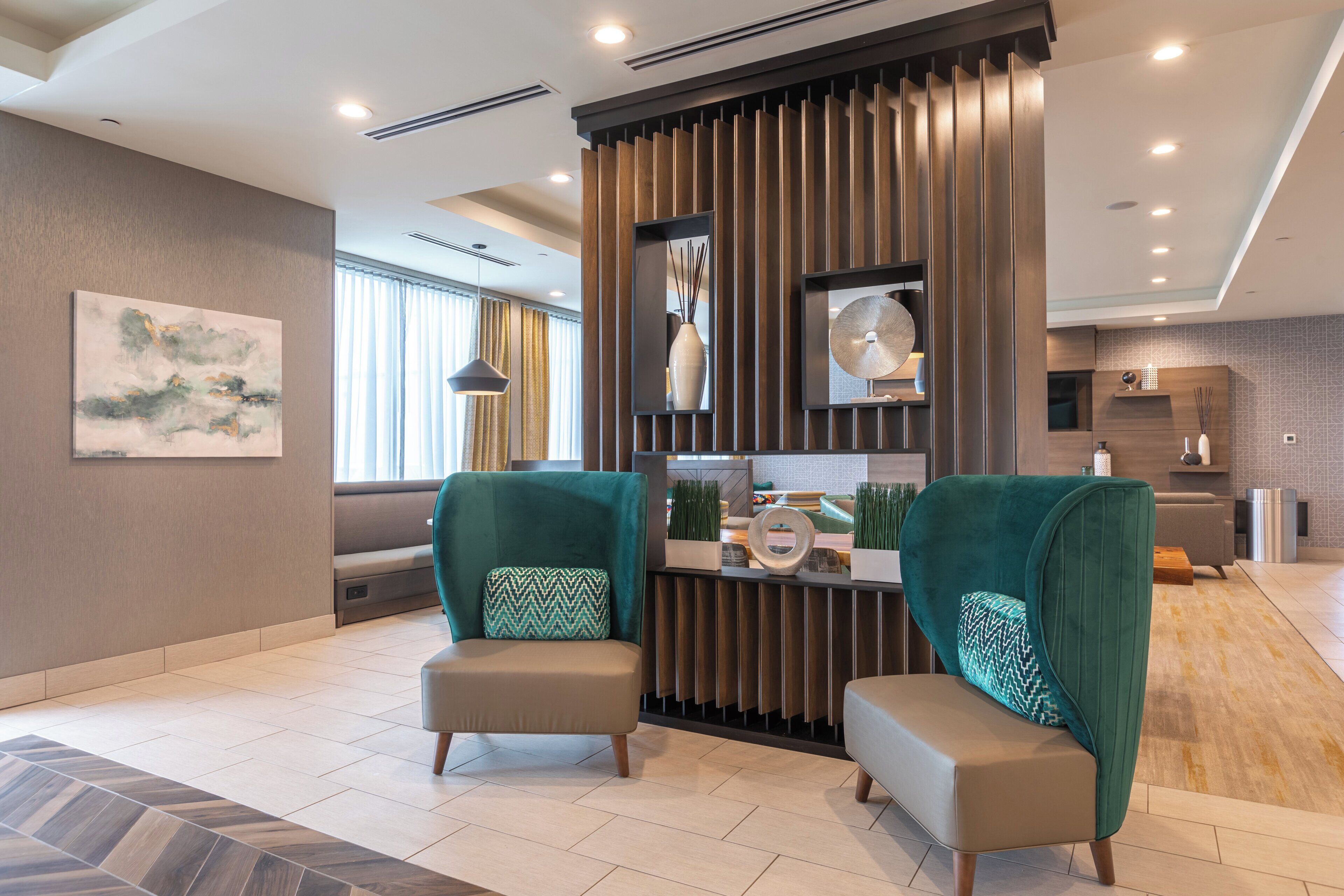 A modern living room with two green armchairs, a wooden partition, and a large abstract painting on the wall.