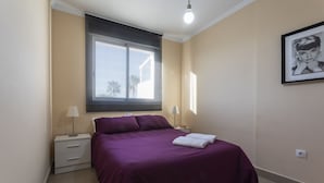 Ein Schlafzimmer mit einem Bett, zwei Nachttischen, einem Fenster mit Jalousien, einem Wandbild und einer Leuchte.