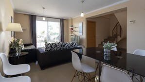 Ein modernes Wohnzimmer mit einem Glastisch, weißen Stühlen, einem schwarzen Sofa und einem großen Fenster mit Vorhängen.