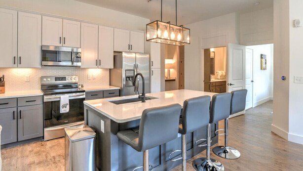 Una cocina moderna con electrodomésticos de acero inoxidable, una isla central con taburetes altos e iluminación colgante.