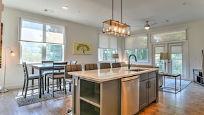Una cocina moderna con una isla central, ventanas amplias y una lámpara colgante.