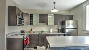 A modern kitchen with dark cabinets, stainless steel appliances, and a central island. - Charming Condo over City Bakery (Asheville)
