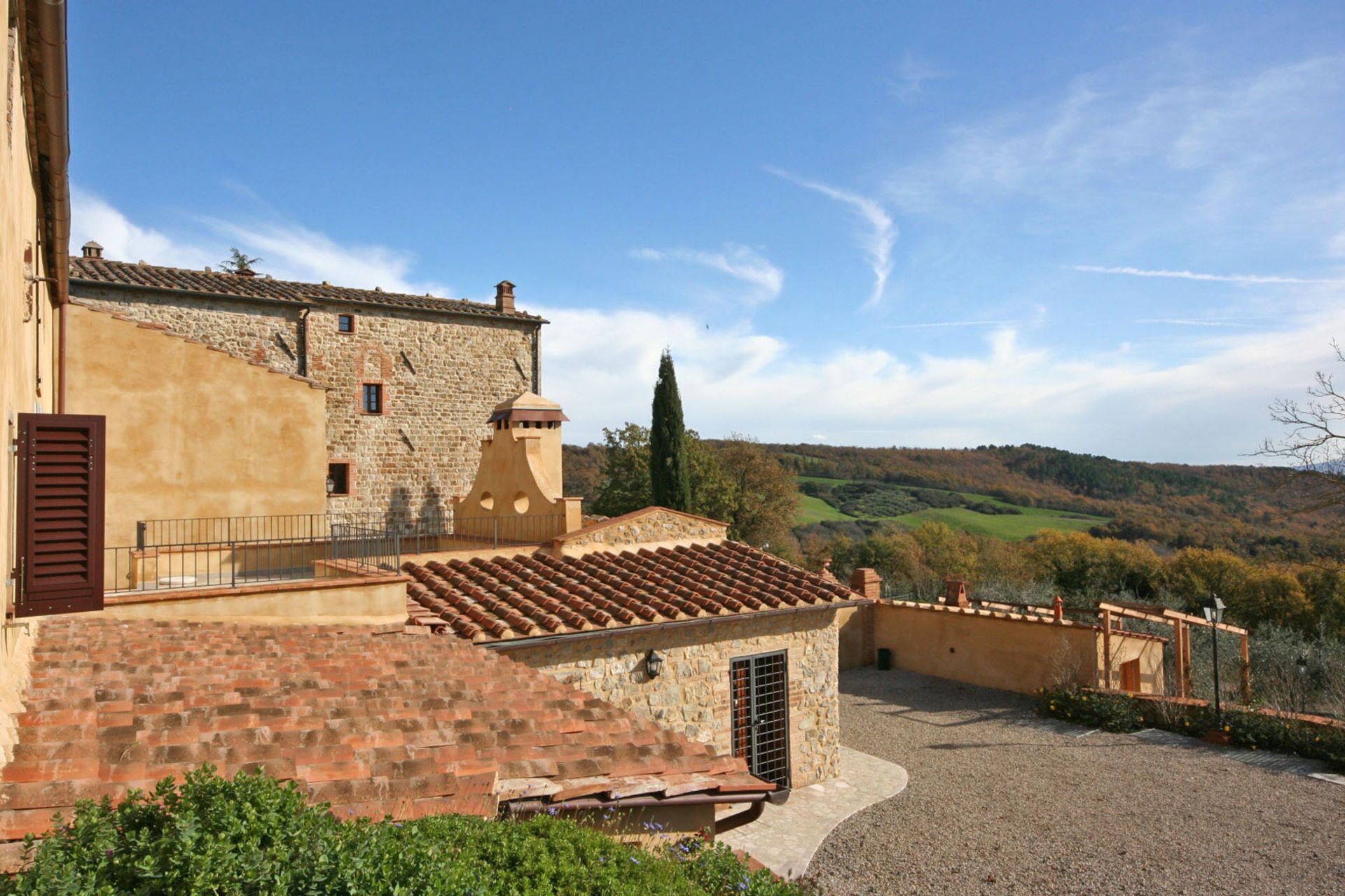 A stone building with a tiled roof, a small garden area, and a view of a hilly landscape.