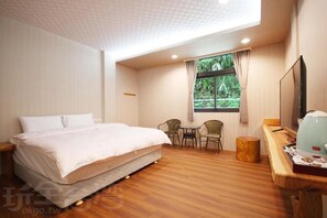 Une chambre d’hôtel avec un lit, une petite table avec des chaises, une fenêtre avec des rideaux et un téléviseur posé sur un meuble en bois.