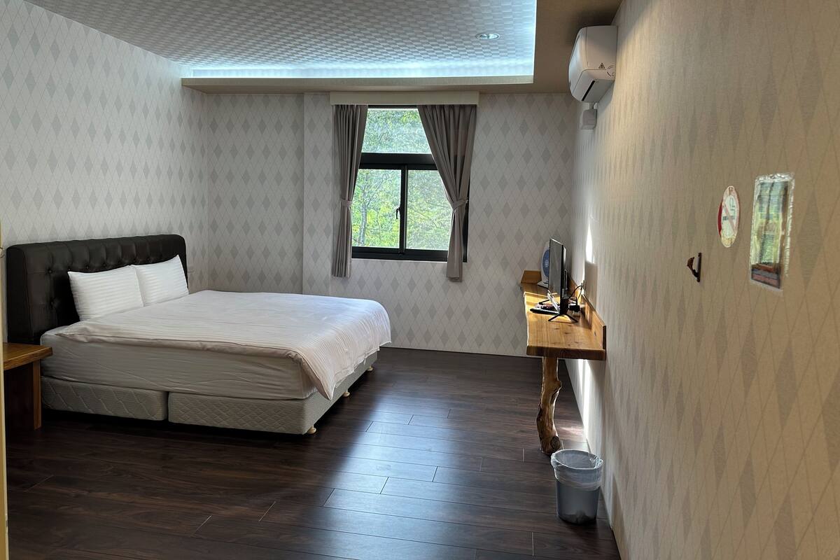 A bedroom with a bed, a desk, and a window.