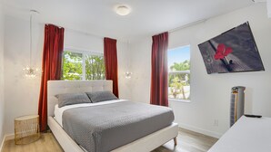 A modern bedroom with a large bed, red curtains, a mounted TV, and a bedside heater.