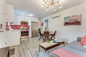 A modern living room with a grey sofa, a coffee table, and a dining area with a table and chairs. - FIFA Perfect 18KM | Rosa: Casita Near Beach & Gym Access (Hollywood)