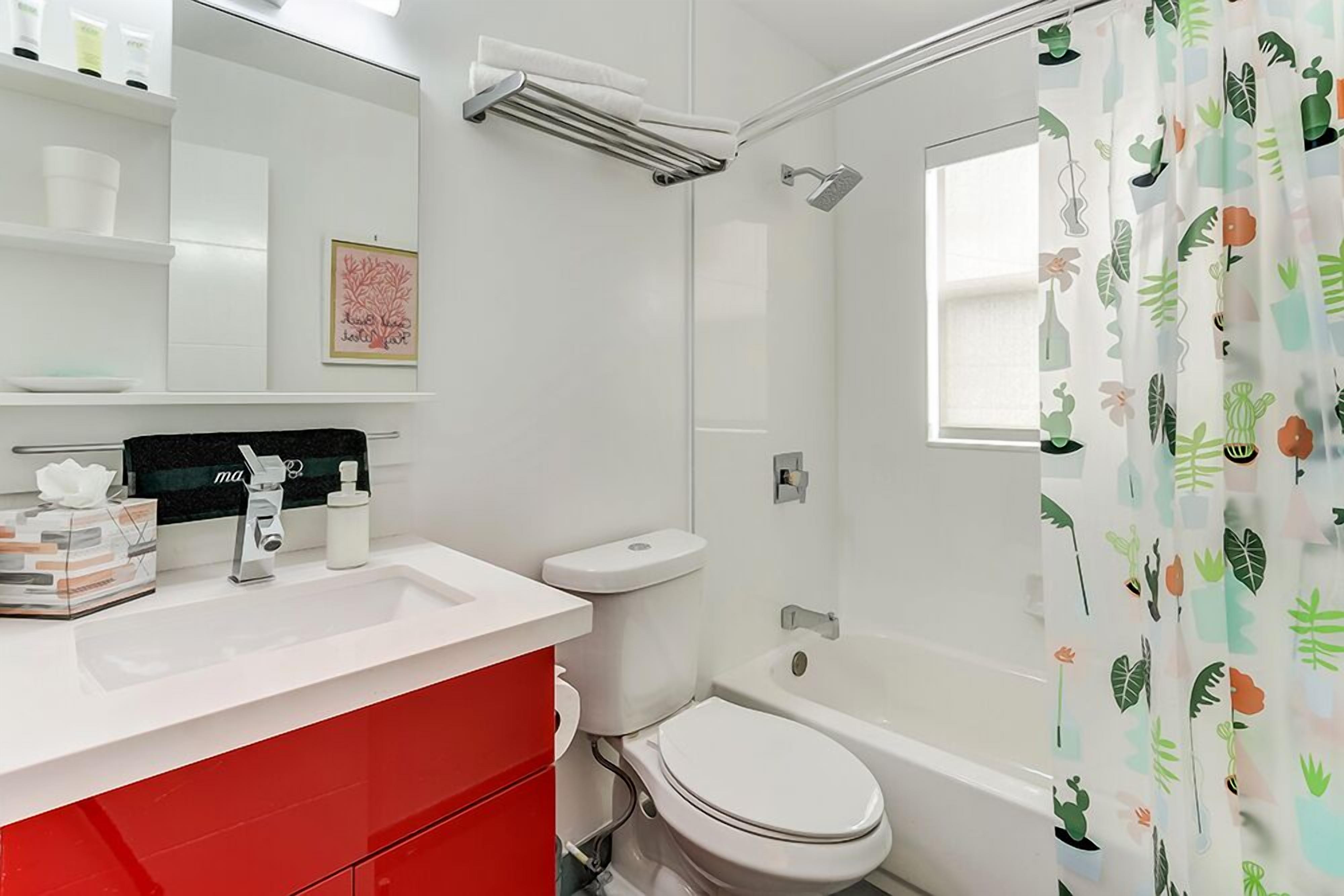 A modern bathroom with a white sink, red vanity, white toilet, and a shower with a glass door.