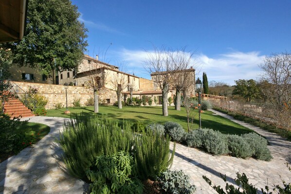 A stone building with a stone staircase leading to a door, surrounded by a well-maintained garden with various shrubs and a clear sky.