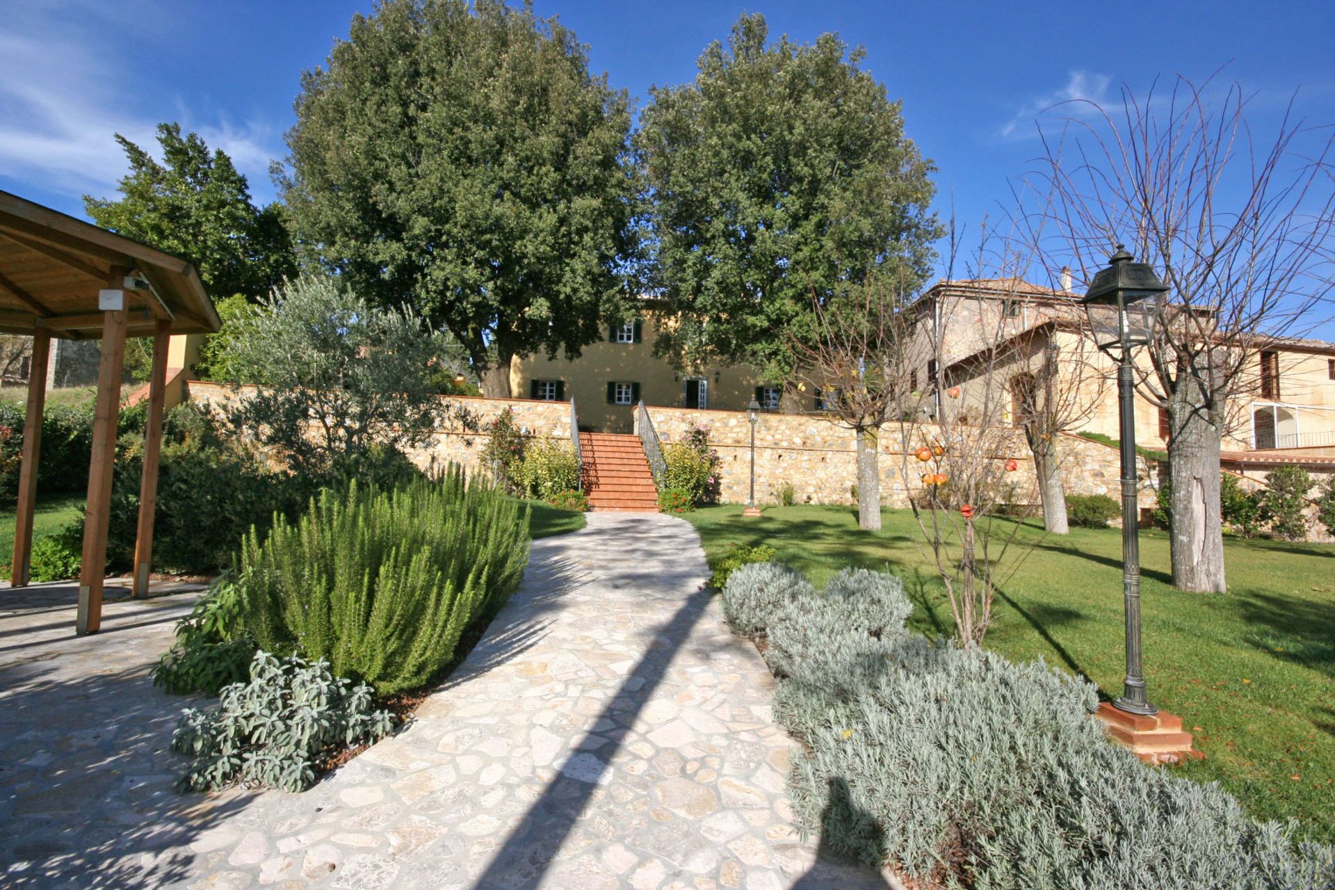 A stone pathway leading to a building with a stone wall and a wooden pergola.
