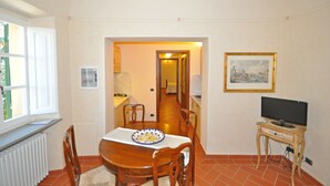 Un comedor con una mesa y sillas de madera, un televisor sobre una mesita y un cuadro en la pared.