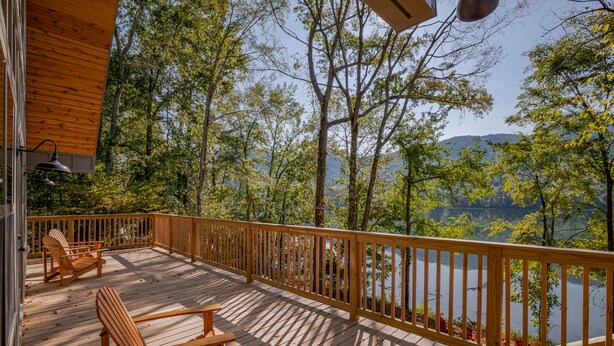 Una terraza de madera con sillas Adirondack y vistas a un lago rodeado de árboles.
