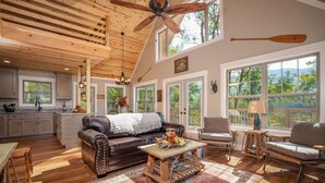 Un amplio salón con techo de madera, chimenea y vistas al exterior.