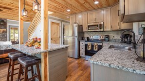 Cocina con techo de madera, encimeras de granito, electrodomésticos de acero inoxidable y una isla central con taburetes.