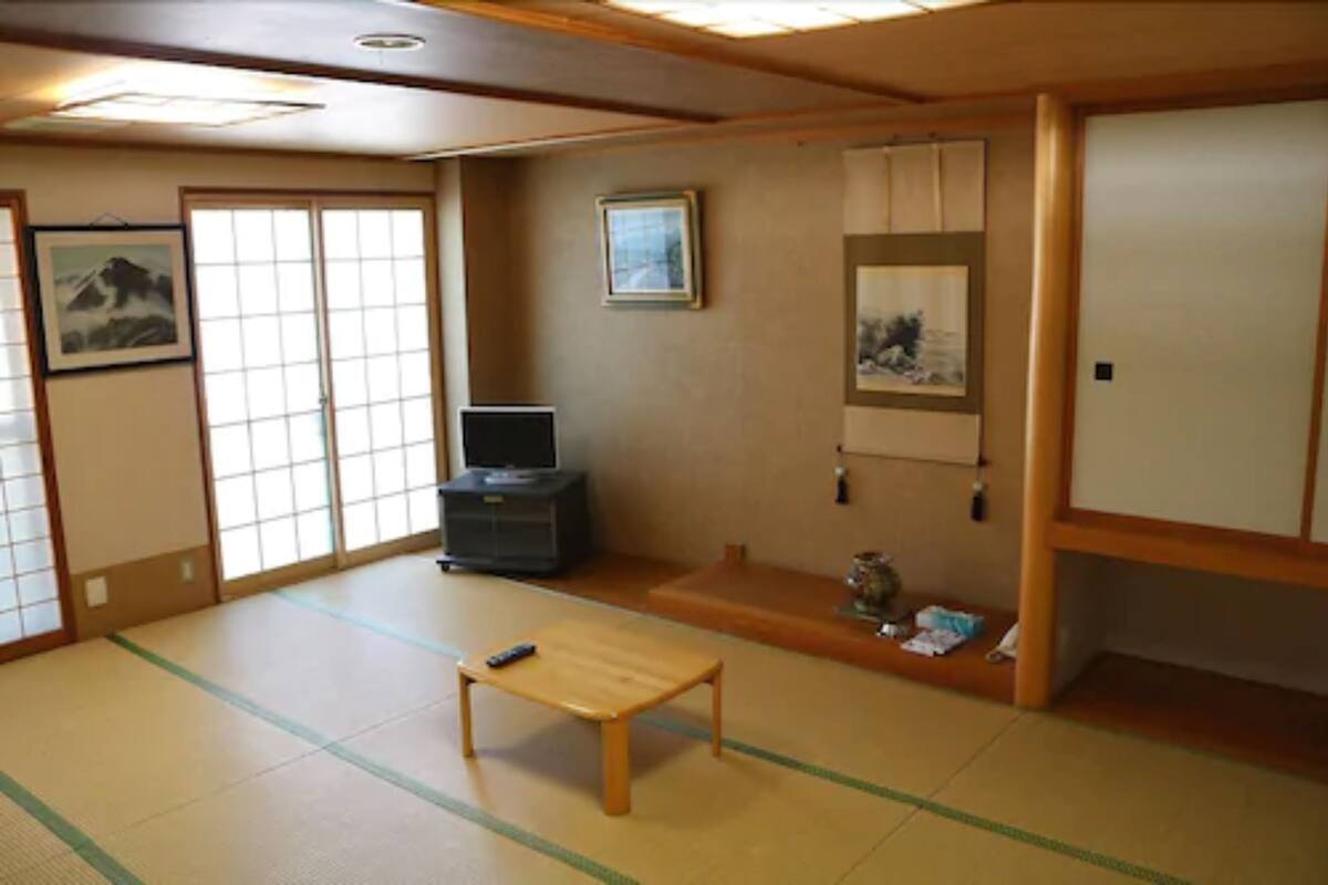 Une pièce de style japonais traditionnel, avec un sol recouvert de tatamis, une basse table en bois, un téléviseur et des portes coulissantes.