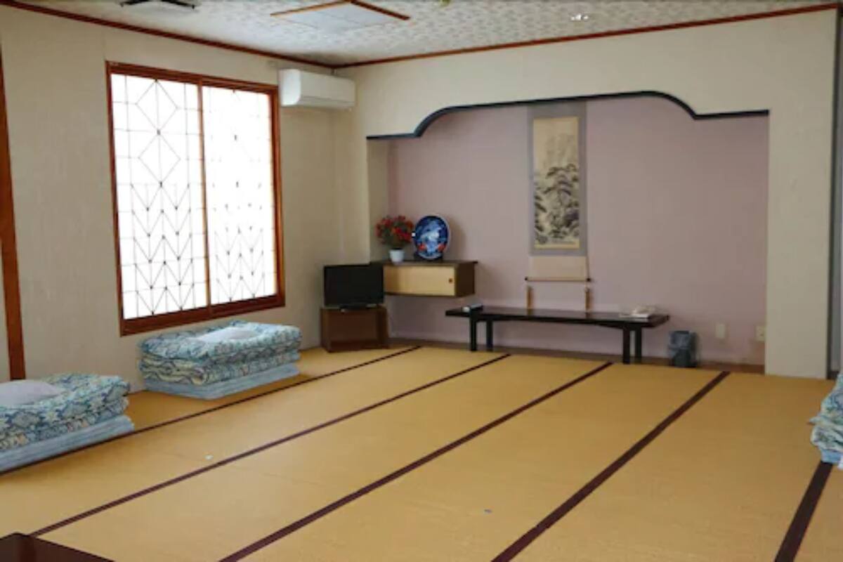 Une pièce avec un sol recouvert de tatamis, comprenant un canapé en tatami, une télévision et une petite table sur laquelle est posée une assiette décorative.