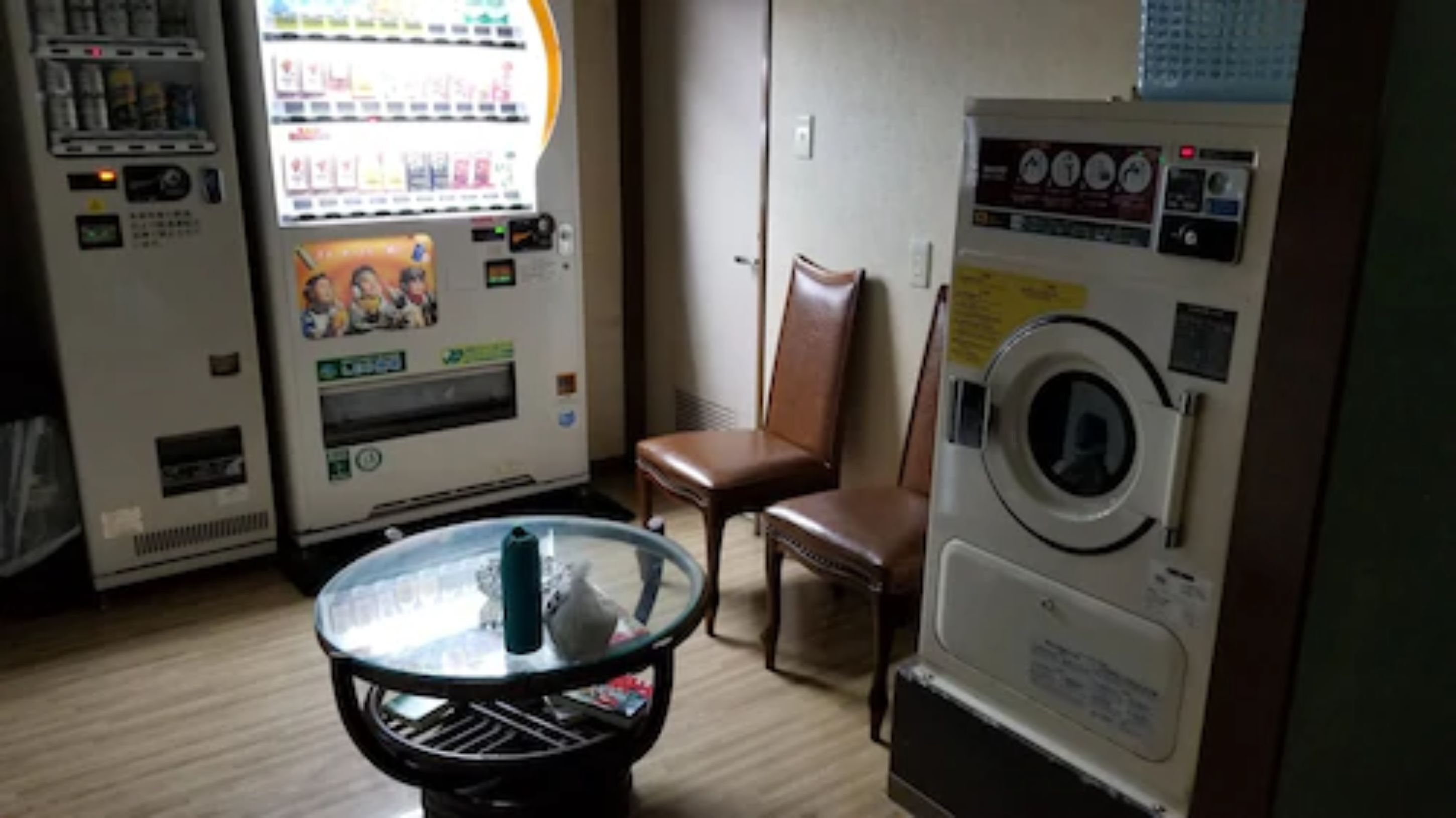 A room with a vending machine, a washing machine, and a glass table.