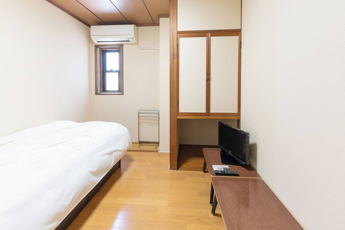Une petite pièce propre, avec un lit, un bureau doté d’un ordinateur et une fenêtre.