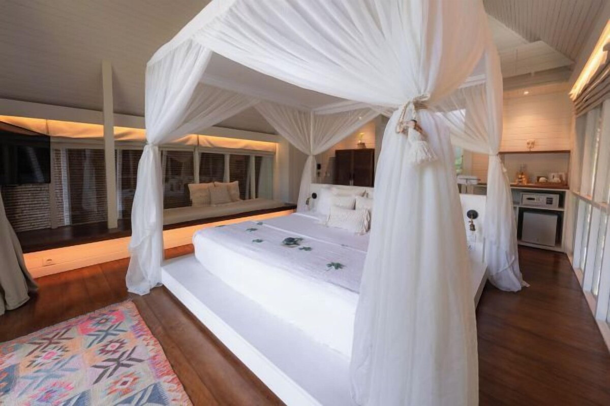 A bedroom with a canopy bed, a small seating area, and a kitchenette.