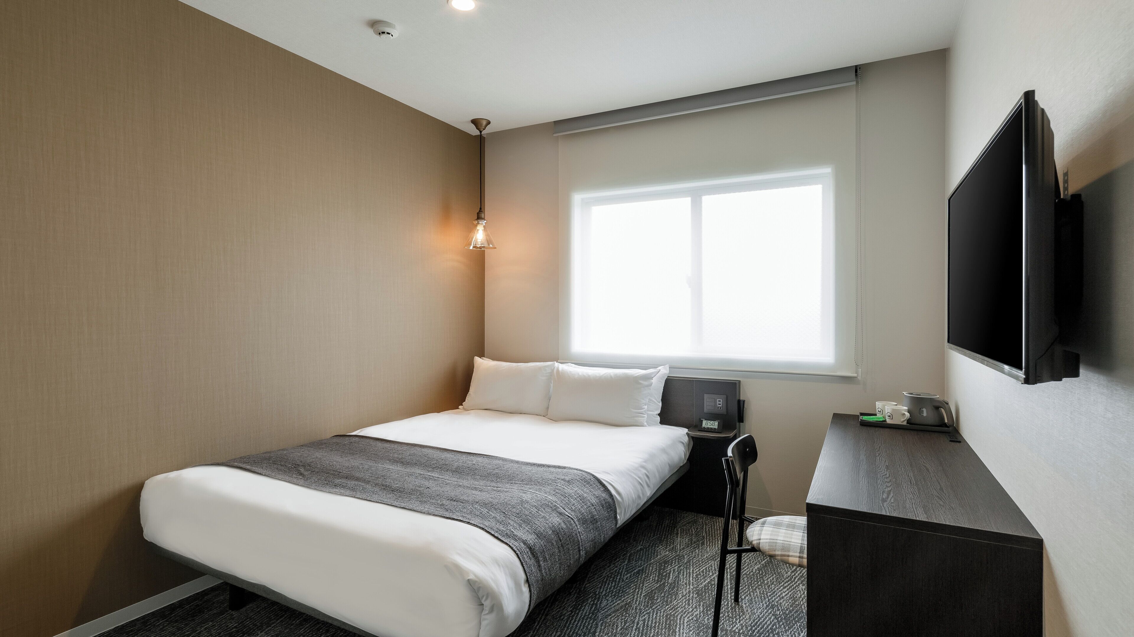 Une chambre d’hôtel avec un lit, un bureau, une chaise, une télévision et une fenêtre.
